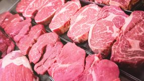 Assortment of fresh red meat cuts, including steaks and roasts, displayed in a butcher shop or supermarket cooler.