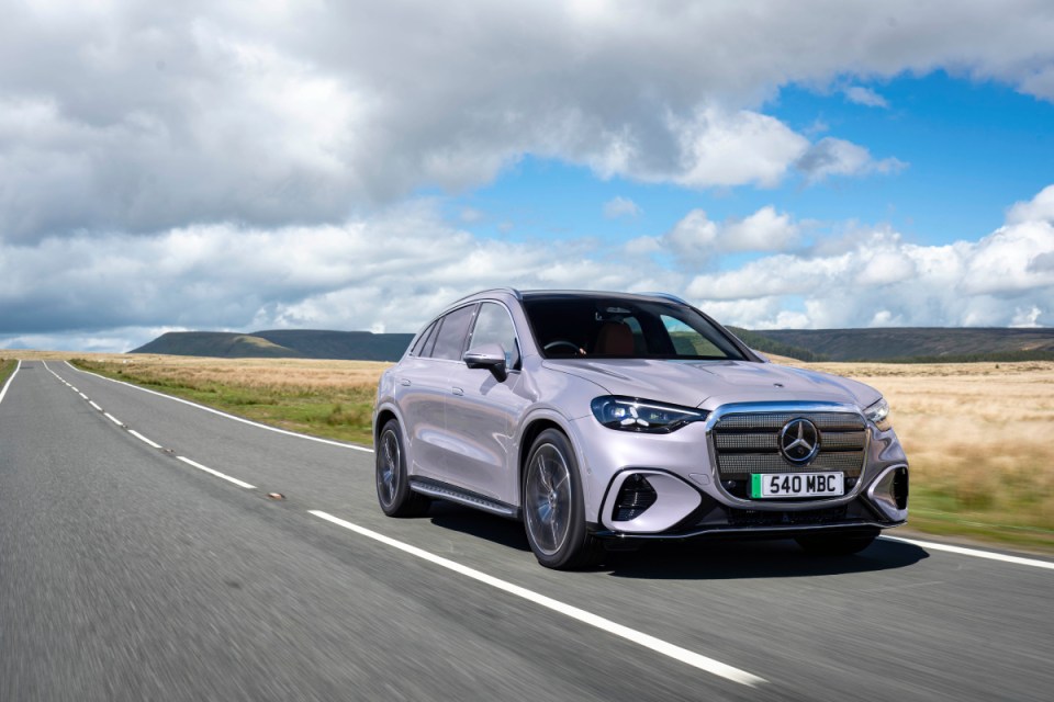 Silver Mercedes-Benz GLC SUV driving on a highway through a rural landscape under a cloudy sky