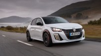 White Peugeot 208 driving on a winding road with mountains and fog in the background