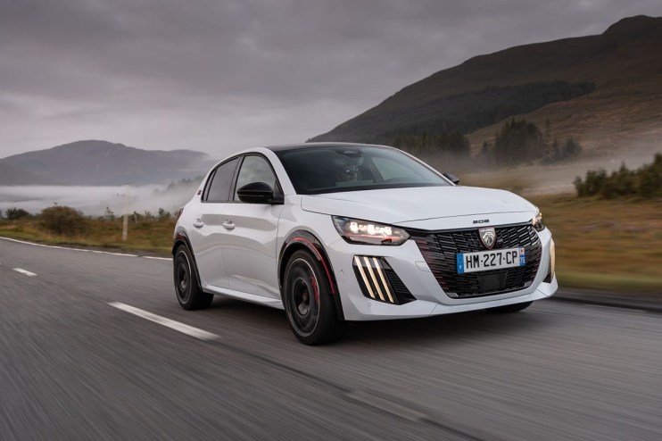 White Peugeot 208 driving on a winding road with mountains and fog in the background