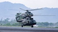 Two military helicopters, dark green, preparing for takeoff on a wet runway with misty mountains in the background