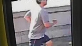 CCTV footage of the Putney Pusher, a man in a grey shirt and black shorts, running past a wall.