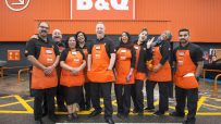 Diverse B&Q team in orange aprons smiling outside a store, representing typical staff.