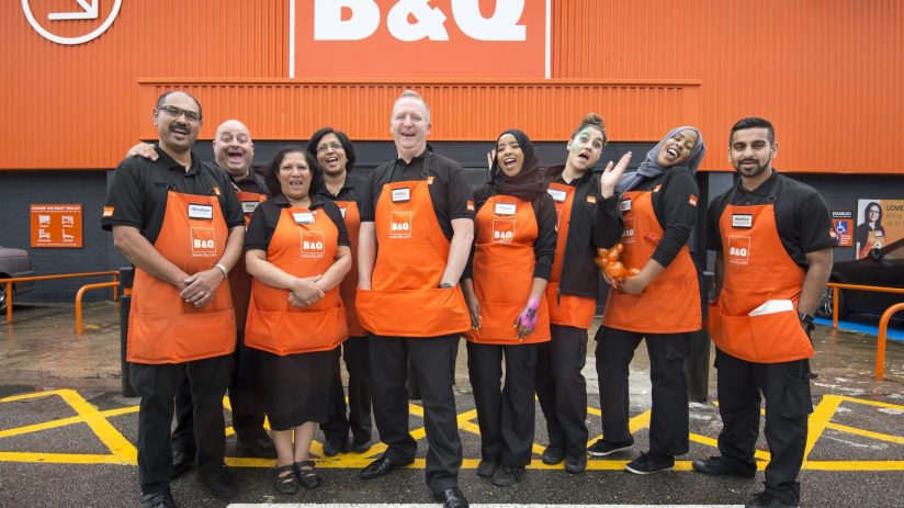 Diverse B&Q team in orange aprons smiling outside a store, representing typical staff.