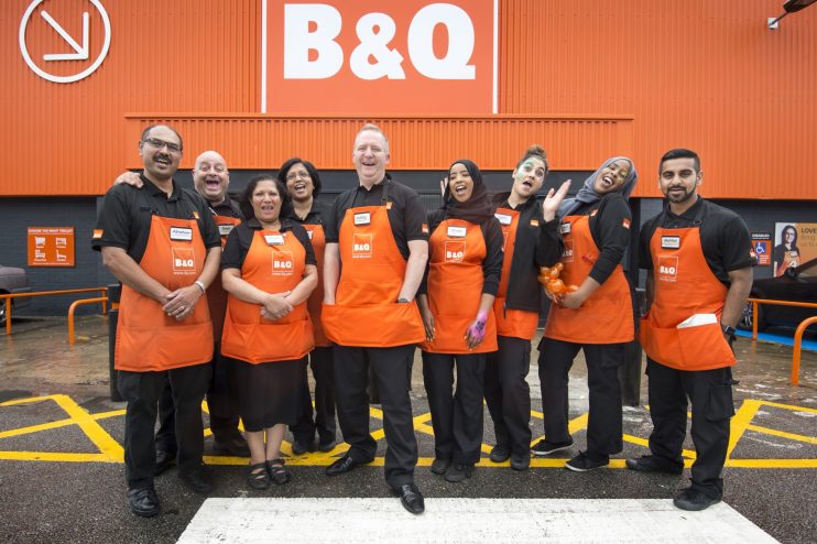 Diverse B&Q team in orange aprons smiling outside a store, representing typical staff.