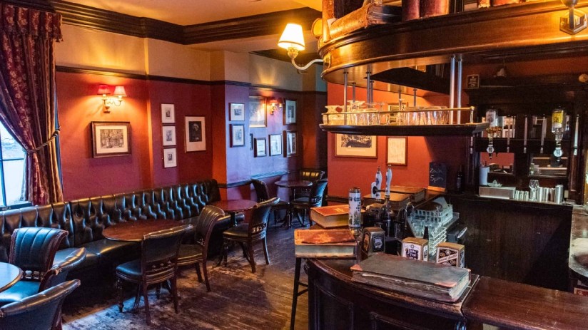 Traditional interior of Ye Olde Cheshire Cheese pub with dark wood, leather seating, and red walls.