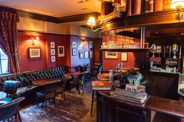 Traditional interior of Ye Olde Cheshire Cheese pub with dark wood, leather seating, and red walls.