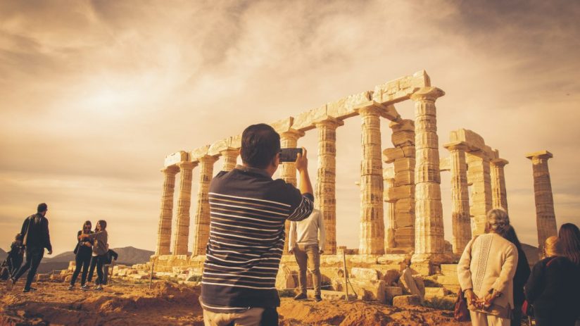 Tourist photographing ancient Greek temple ruins with Doric columns under a dramatic sky, Acropolis, Athens