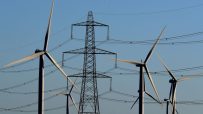 Wind turbines and electricity pylon against a clear blue sky, illustrating renewable energy and power transmission.