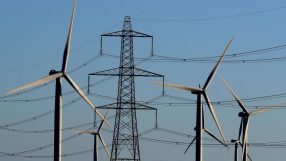 Wind turbines and electricity pylon against a clear blue sky, illustrating renewable energy and power transmission.