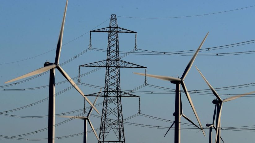 Wind turbines and electricity pylon against a clear blue sky, illustrating renewable energy and power transmission.