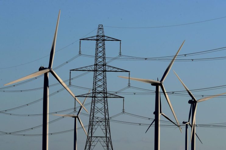 Wind turbines and electricity pylon against a clear blue sky, illustrating renewable energy and power transmission.
