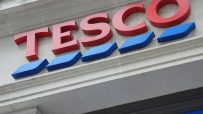 Tesco store sign with red letters and blue wavy lines, visible on a building facade