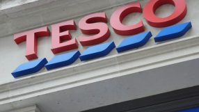 Tesco store sign with red letters and blue wavy lines, visible on a building facade