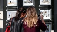 Two women view real estate listings in a Parkheath agency window, one taking a photo with her phone.