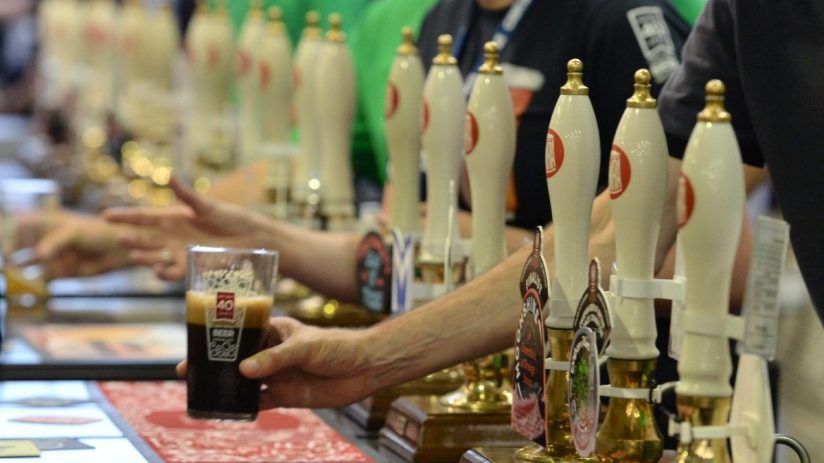 Person holding a glass of dark beer near multiple beer taps at a brewery or bar.
