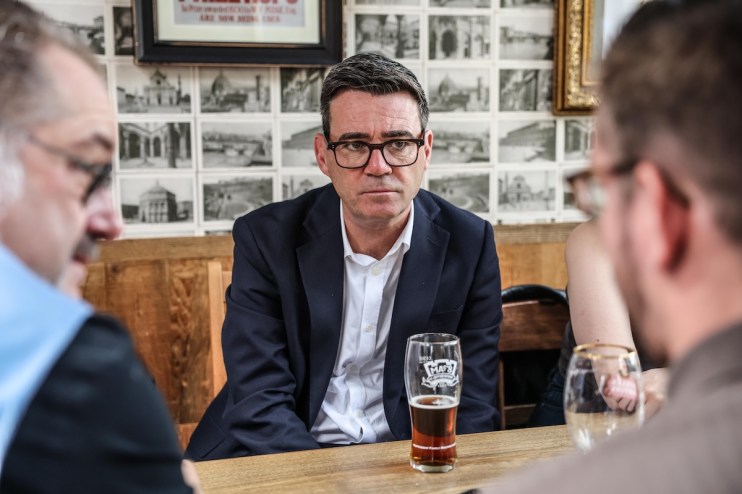 Andy Burnham, Mayor of Greater Manchester, in a dark suit and glasses, sitting at a table with a beer.