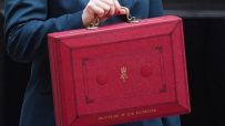 Woman in a teal suit holding the red Chancellor of the Exchequer box outside Downing Street.