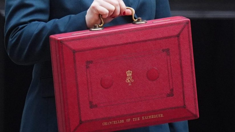 Woman in a teal suit holding the red Chancellor of the Exchequer box outside Downing Street.