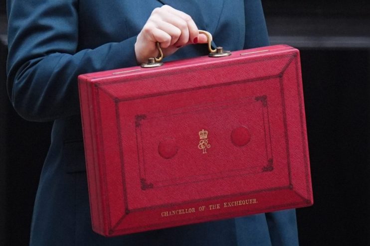 Woman in a teal suit holding the red Chancellor of the Exchequer box outside Downing Street.