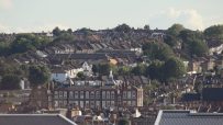 Dense residential area with traditional brick houses and lush green trees under a clear sky.