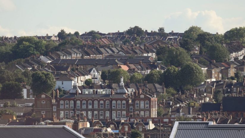 Dense residential area with traditional brick houses and lush green trees under a clear sky.