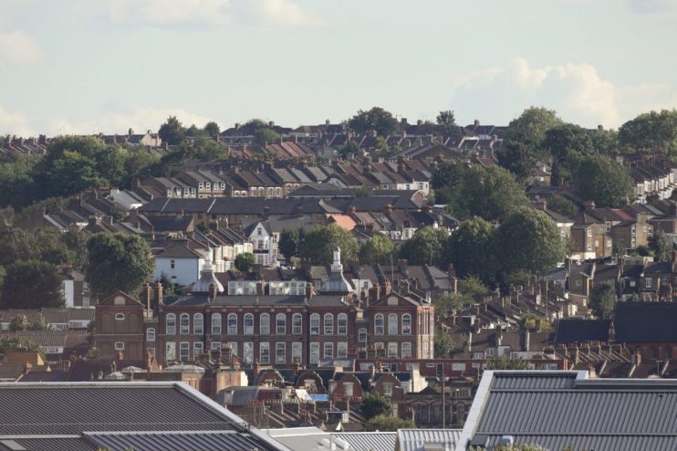 Dense residential area with traditional brick houses and lush green trees under a clear sky.
