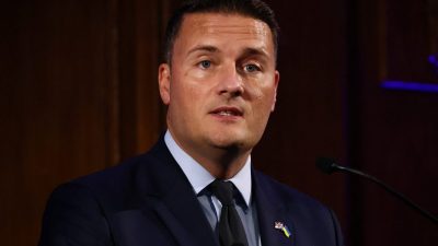 Wes Streeting, Shadow Health Secretary, speaking at a podium with UK and Ukraine flag pins on his lapel.