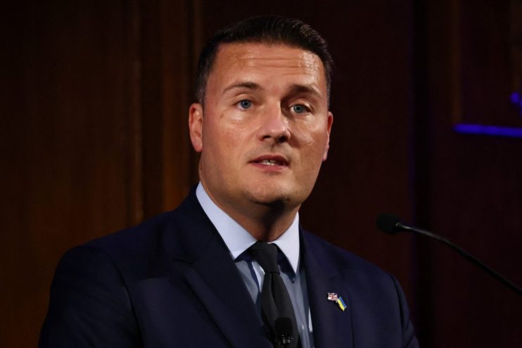 Wes Streeting, Shadow Health Secretary, speaking at a podium with UK and Ukraine flag pins on his lapel.