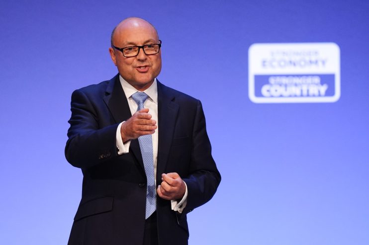Man in suit and glasses speaking at a podium with a Stronger Economy, Stronger Country sign.