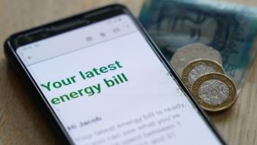 Smartphone displaying an energy bill email with UK currency (pound coins and banknote) on a wooden table.