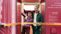 Two men cut a flame-themed ribbon at the entrance of the Monument Micro Museum, a Great Fire of London exhibit.