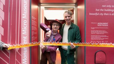 Two men cut a flame-themed ribbon at the entrance of the Monument Micro Museum, a Great Fire of London exhibit.