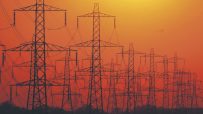 Multiple electricity pylons silhouetted against an orange sunset sky, symbolizing energy infrastructure.