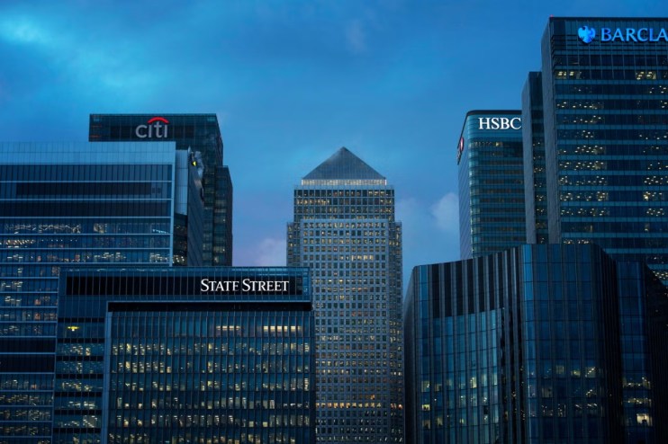 Financial district skyline with illuminated corporate buildings for Citi, State Street, HSBC, and Barclays against a blue ...