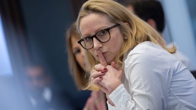 Blonde woman in glasses with finger to lips, a quiet gesture, in a professional meeting setting.