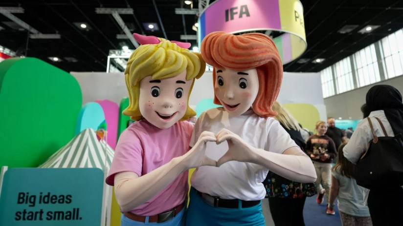 Two cartoon mascots, one blonde and one redhead, forming a heart with their hands at an IFA event