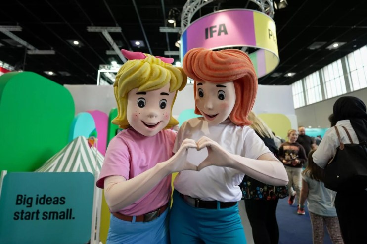 Two cartoon mascots, one blonde and one redhead, forming a heart with their hands at an IFA event