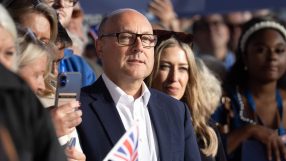 Andrew Griffith, Conservative MP, in glasses and dark suit, holding a Union Jack flag at an event.