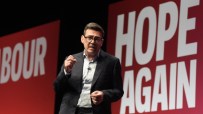 Andy Burnham speaking at the Labour conference, with red HOPE AGAIN and LABOUR banners in background.