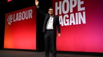 Andy Burnham waving on stage at a Labour Party Conference with HOPE AGAIN slogan visible
