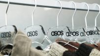 Clear acrylic Asos hangers with black logos holding various garments on a clothing rail