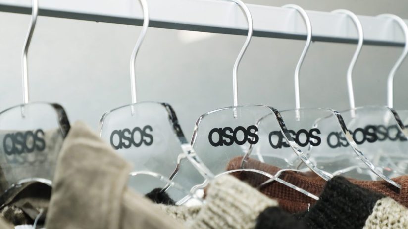 Clear acrylic Asos hangers with black logos holding various garments on a clothing rail