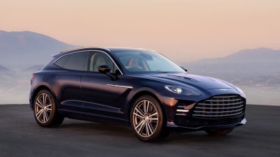 Dark blue Aston Martin DBX SUV parked outdoors with mountains and a sunset sky in the background.