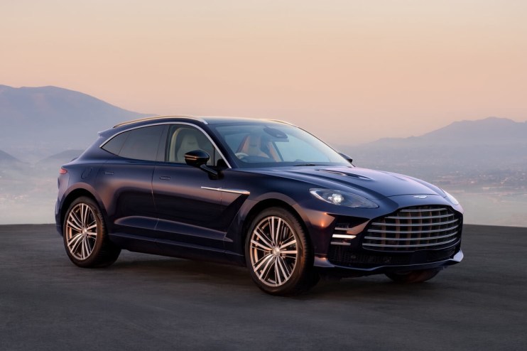 Dark blue Aston Martin DBX SUV parked outdoors with mountains and a sunset sky in the background.