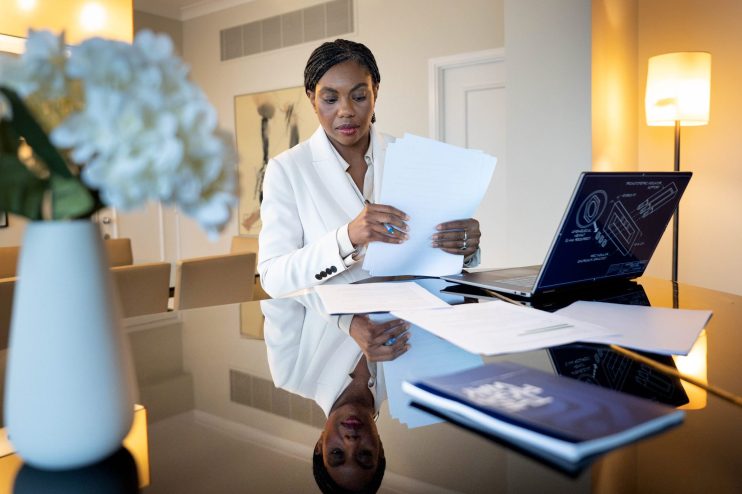 Kemi Badenoch, Secretary of State for Business and Trade, preparing for a conference speech, reviewing documents at a desk.
