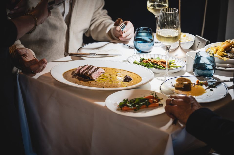 Elegant dining table with sliced steak, asparagus, carrots, wine, and water glasses at Bagatelle restaurant.