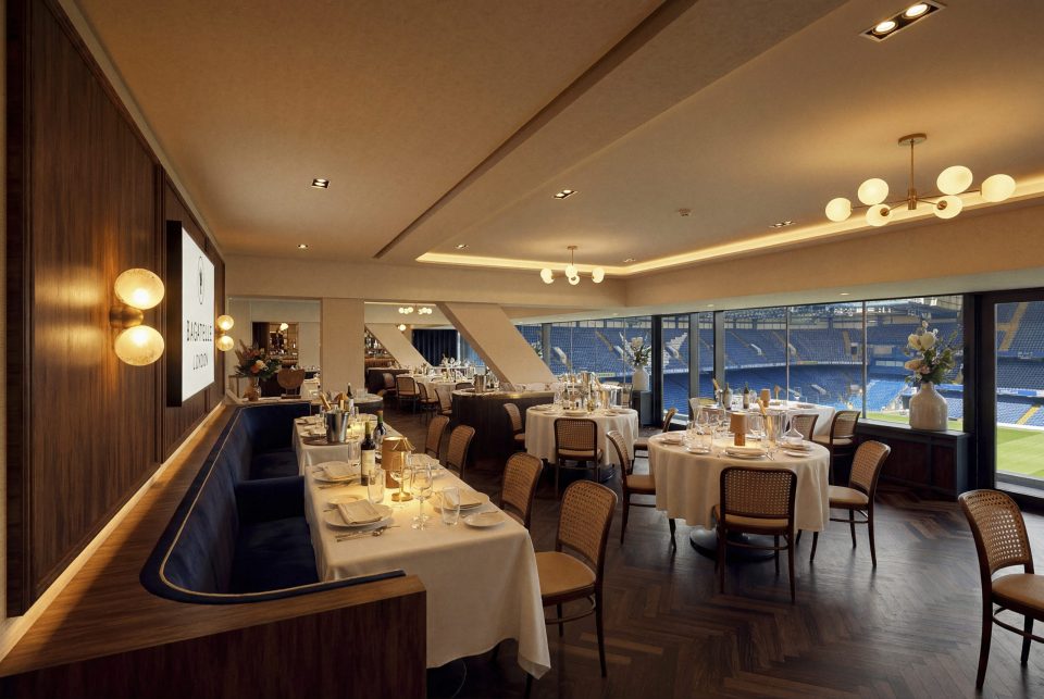 Elegant Bagatelle London restaurant interior with stadium view, set tables, blue banquettes, and modern lighting.