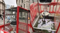 Art installation resembling a red phone box with IN CASE OF EMERGENCY INFLATION BREAK GLASS and money inside.