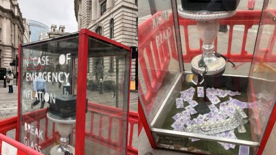 Art installation resembling a red phone box with IN CASE OF EMERGENCY INFLATION BREAK GLASS and money inside.
